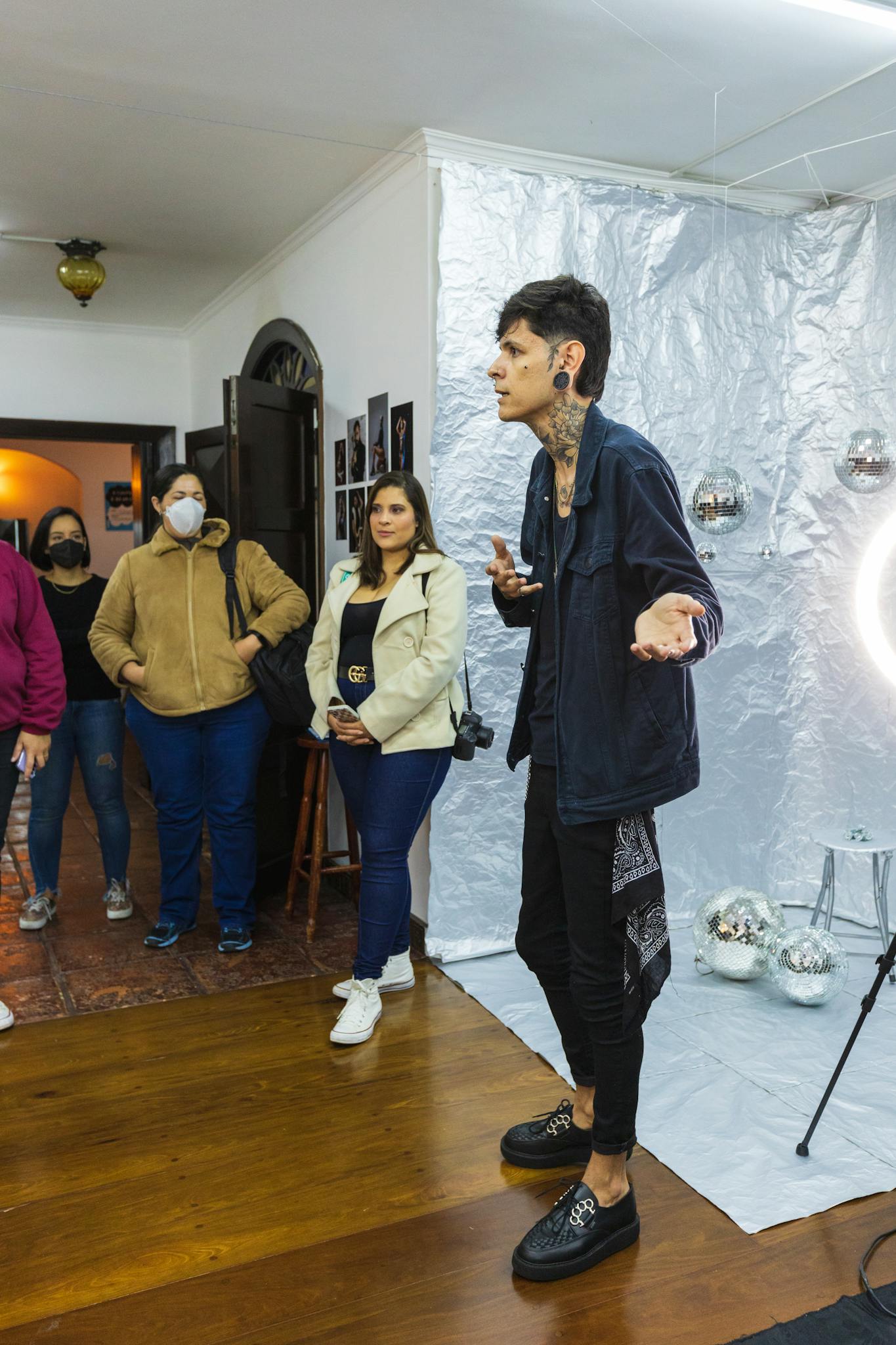 A diverse group attends an art seminar indoors, featuring a speaker in front of a metallic backdrop.