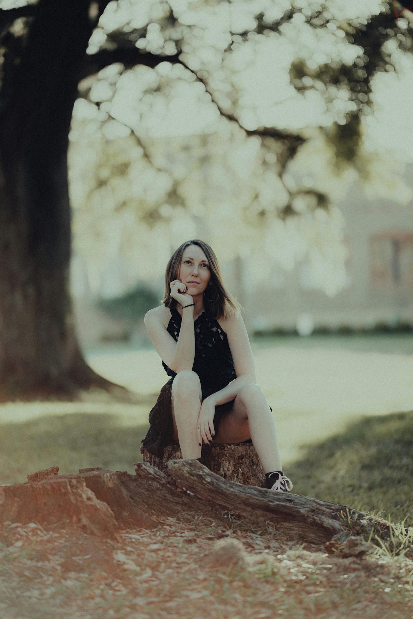A serene portrait of a woman seated on a log in a sunlit park, embodying tranquility.